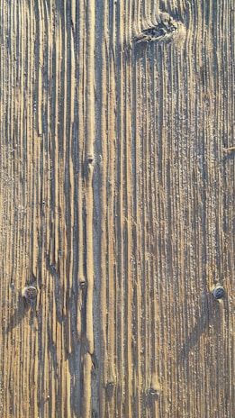 Close-up view of a wooden surface with distinct vertical grooves and textured patterns. The wood shows natural signs of wear, including knots and weathering marks.