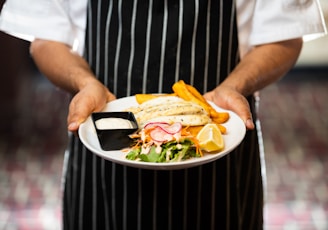 a chef holding a plate with a sandwich and chips
