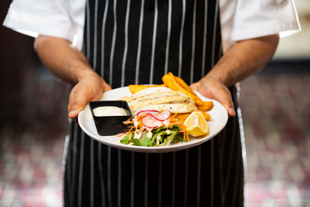 Un chef sosteniendo un plato con un sándwich y papas fritas
