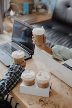 A close-up of hands collaborating over a laptop with HR documents and coffee cups.