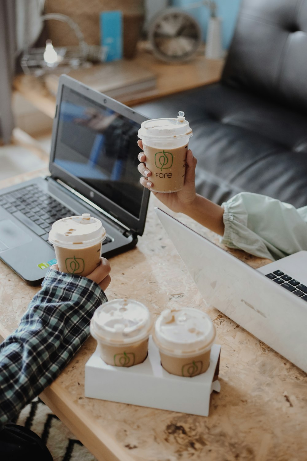 two persons holding drinks beside table with drinks and laptops