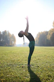 A person gracefully performing the tree pose outdoors with sunlight filtering through leaves.
