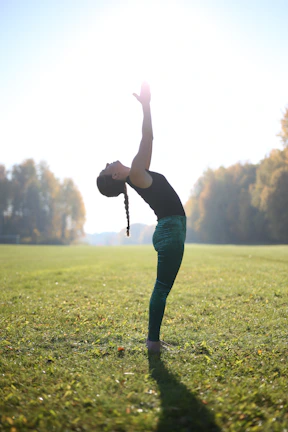 A person gracefully performing the tree pose outdoors with sunlight filtering through leaves.
