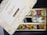 An open box of assorted traditional Indian sweets, known as mithai, with a variety of bright and colorful pieces arranged neatly in compartments. The box displays elegant gold floral designs and inscriptions, with the label 'Dryfruit Sweets Premium 24 Carats Mithai Magic' on the lid.
