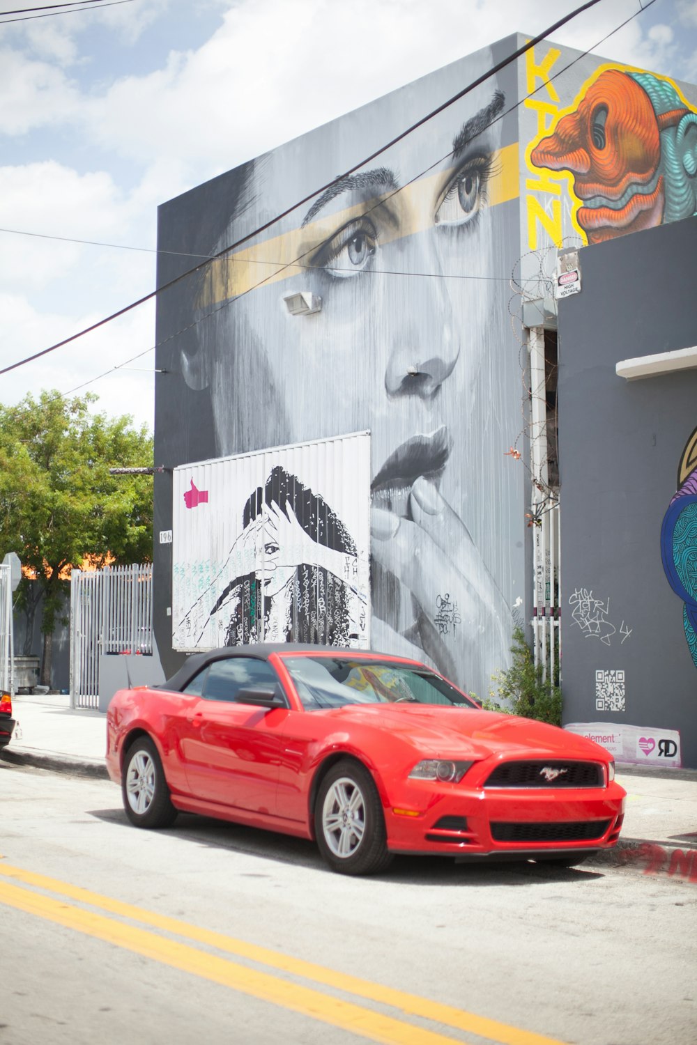 red and black Ford Mustang coupe parked beside building with graffiti during daytime