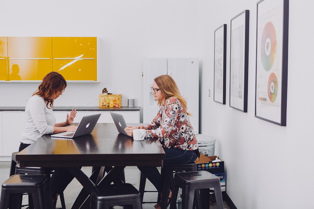 2 women using laptop by table