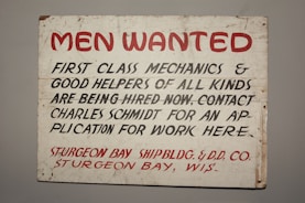 A vintage sign with bold red and black lettering on a white background. The text advertises job openings for first-class mechanics and helpers, with instructions to contact Charles Schmidt for an application. The bottom features the name of a shipbuilding and dry dock company located in Sturgeon Bay, Wisconsin.
