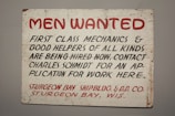 A vintage sign with bold red and black lettering on a white background. The text advertises job openings for first-class mechanics and helpers, with instructions to contact Charles Schmidt for an application. The bottom features the name of a shipbuilding and dry dock company located in Sturgeon Bay, Wisconsin.