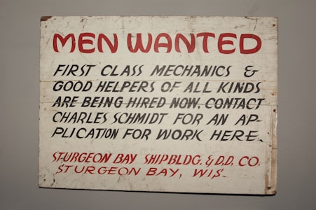 A vintage sign with bold red and black lettering on a white background. The text advertises job openings for first-class mechanics and helpers, with instructions to contact Charles Schmidt for an application. The bottom features the name of a shipbuilding and dry dock company located in Sturgeon Bay, Wisconsin.