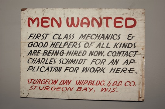 A vintage sign with bold red and black lettering on a white background. The text advertises job openings for first-class mechanics and helpers, with instructions to contact Charles Schmidt for an application. The bottom features the name of a shipbuilding and dry dock company located in Sturgeon Bay, Wisconsin.