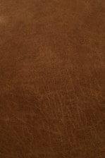 A close-up view of a textured, brown leather surface with visible grain and natural patterns.