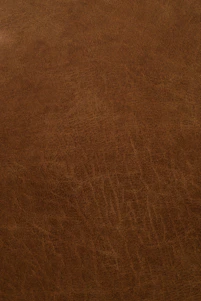Close-up of rich, dark brown leather being carefully inspected by a skilled craftsman in a well-lit workshop.
