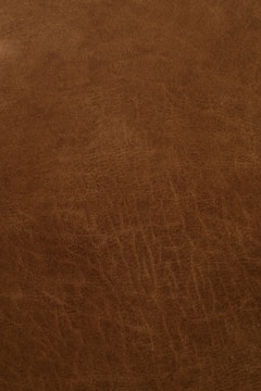 A close-up view of a textured, brown leather surface with visible grain and natural patterns.