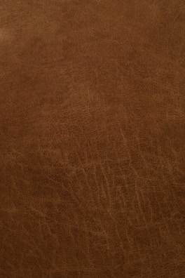 A close-up view of a textured, brown leather surface with visible grain and natural patterns.