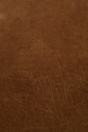 A close-up view of a textured, brown leather surface with visible grain and natural patterns.
