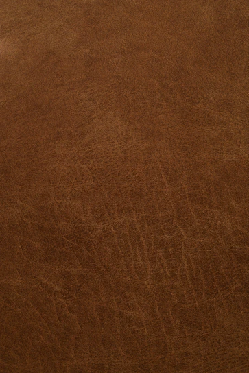 Close-up of rich, dark brown leather being carefully inspected by a skilled craftsman in a well-lit workshop.