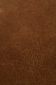 A close-up view of a textured, brown leather surface with visible grain and natural patterns.