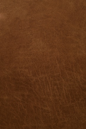 A close-up view of a textured, brown leather surface with visible grain and natural patterns.