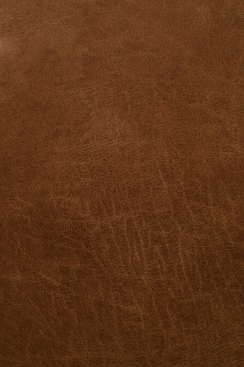 A close-up view of a textured, brown leather surface with visible grain and natural patterns.