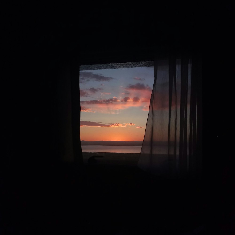 cortina de ventana con vista al agua del mar durante la puesta de sol
