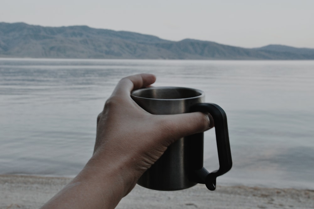 person holding gray stainless steel mug