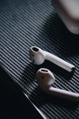 AirPods resting on a black surface with subtle yellow lighting highlighting their shape.