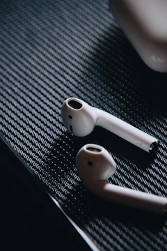 AirPods resting on a black surface with subtle yellow lighting highlighting their shape.