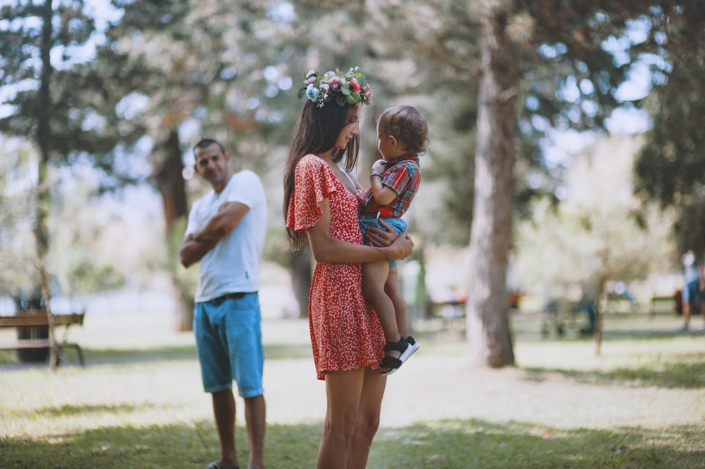 woman carrying toddler standing beside man during daytime