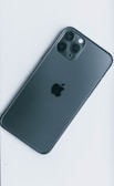 A sleek smartphone with a dark gray finish, featuring three camera lenses on the upper left corner and an apple logo in the center.