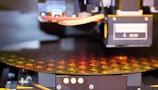 Close-up of a technician inspecting a semiconductor wafer under bright lab lights.