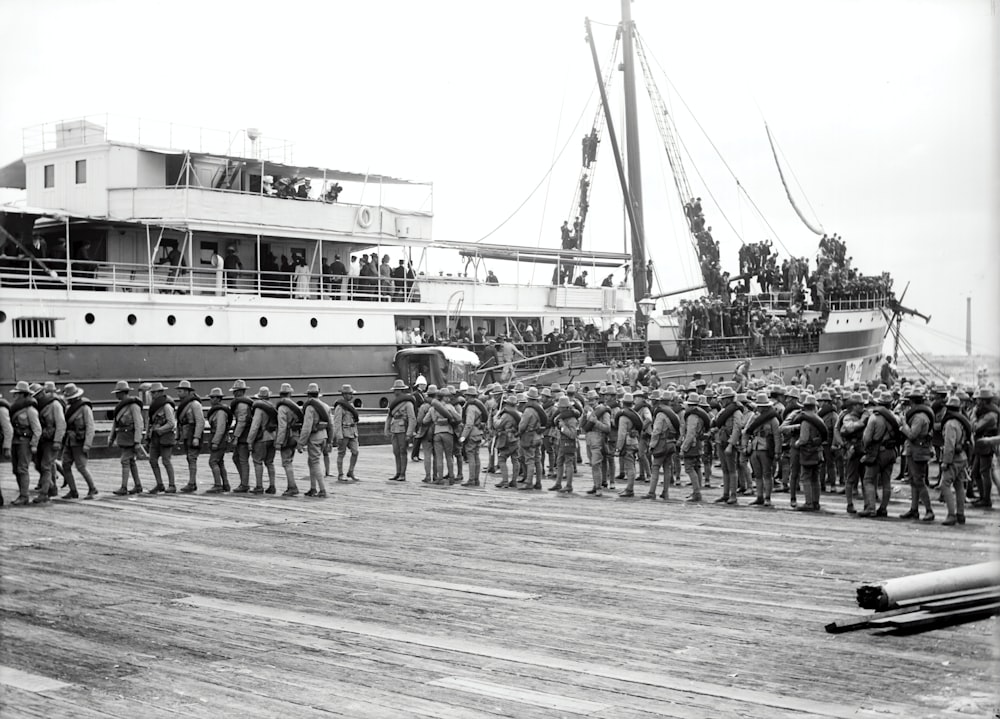 Photographie en niveaux de gris d’un soldat marchant à côté d’un navire à passagers