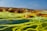 A striking landscape with vibrant yellow and green mineral deposits on the ground, surrounding pools of clear water. Rocky formations are scattered throughout the scene under a clear blue sky, creating a surreal and otherworldly appearance.