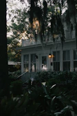 Twilight view of a historic home with warm lights glowing inside and Spanish moss hanging from nearby trees.