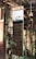 A wooden signboard hanging in a rustic setting, with handwritten text listing items such as handmade crafts, clothes, accessories, wind chimes, books, and pots & plants. The background includes bamboo and other wooden structures, giving a cozy and natural ambiance.