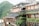 A multi-level building adorned with vibrant greenery and traditional red lanterns, set against a lush mountainous backdrop. The structure features wooden accents and open balconies, creating a harmonious blend with nature.