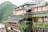 A multi-level building adorned with vibrant greenery and traditional red lanterns, set against a lush mountainous backdrop. The structure features wooden accents and open balconies, creating a harmonious blend with nature.