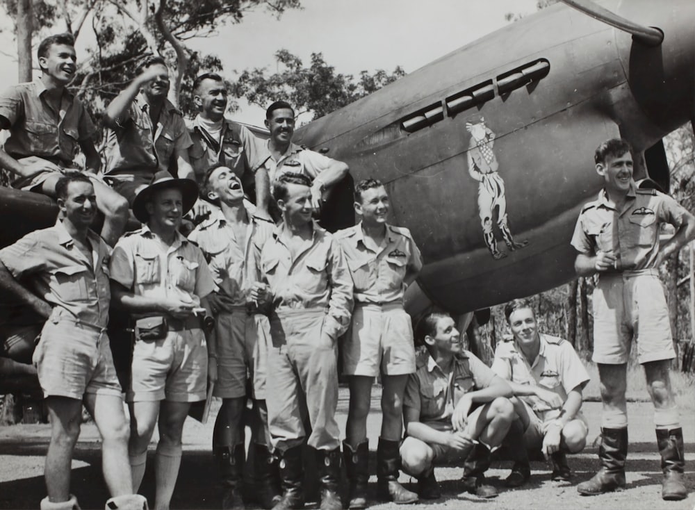 grayscale photography of group of men beside fighter jet