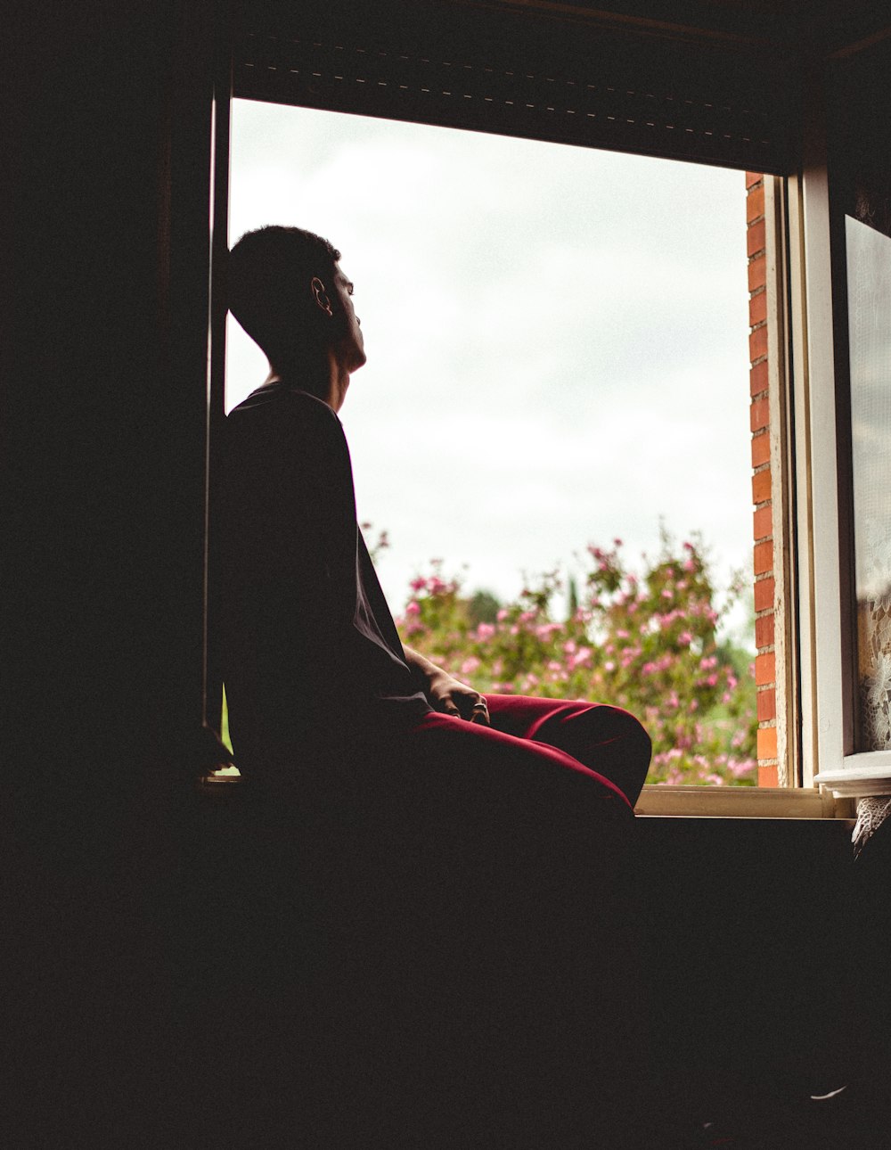 a person sitting on a window sill looking out the window