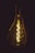 A glowing light bulb with visible filament emits a warm, golden light against a dark background. The intricate design of the filament is prominently displayed, creating a sense of vintage style and ambiance.