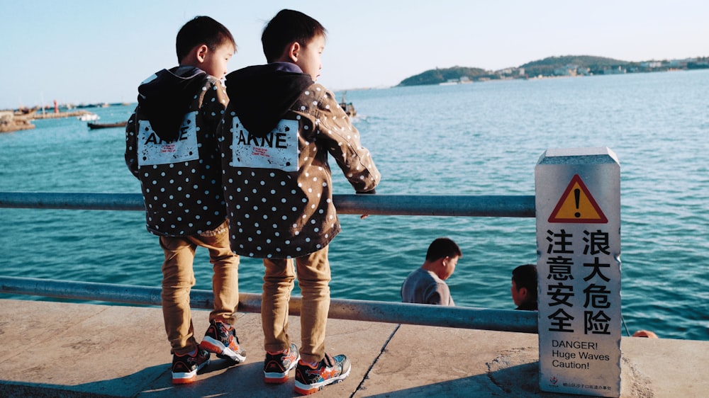 a couple of kids standing next to a body of water