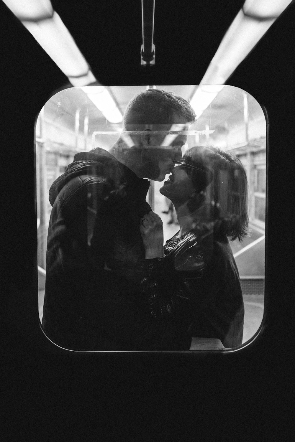 couple standing on window in grayscale photography