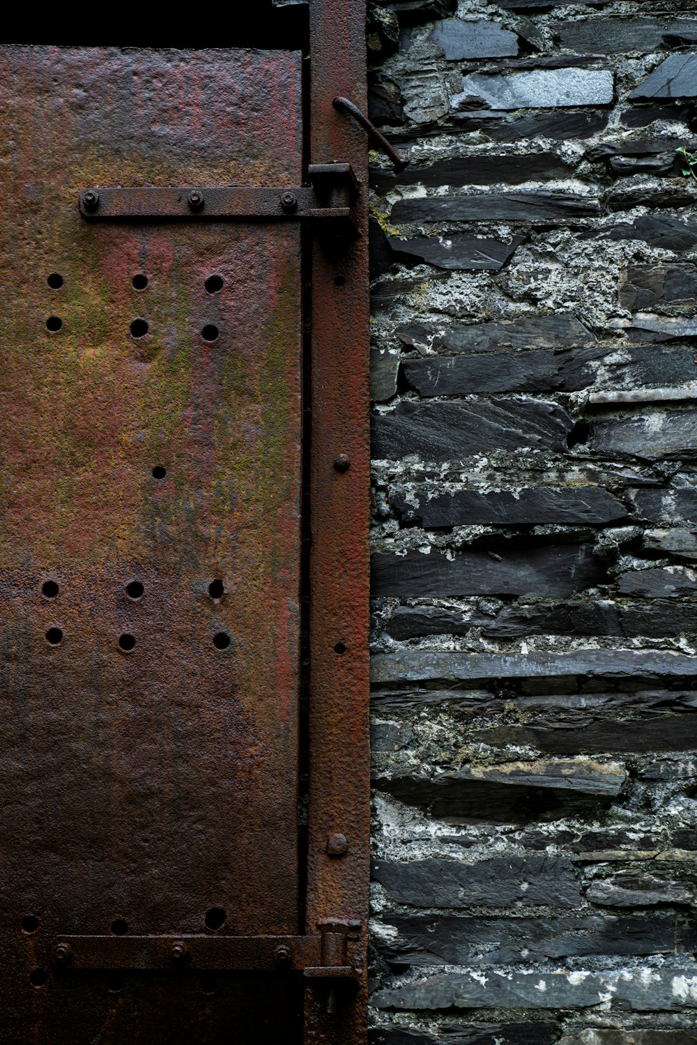 a rusted metal door in front of a stone wall
