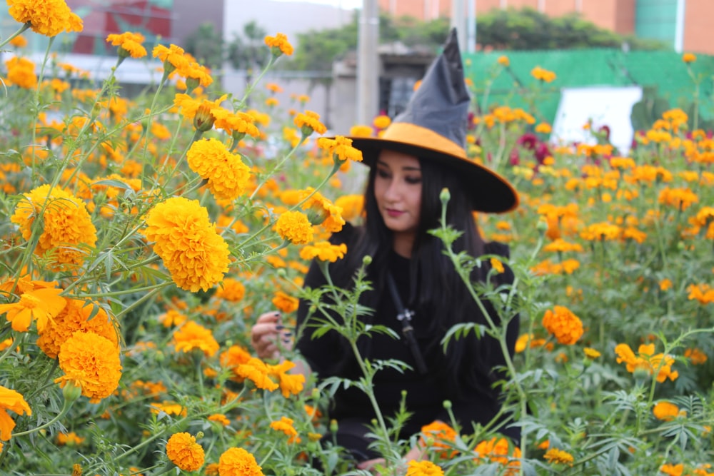 Mujer vestida con traje de bruja negro y amarillo caminando sobre flor amarilla de la pradera