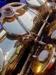 Close-up view of a brass instrument with detailed focus on the mechanism and keys, revealing polished, reflective surfaces with some signs of wear. The intricate parts are captured in warm lighting, highlighting the metallic texture.