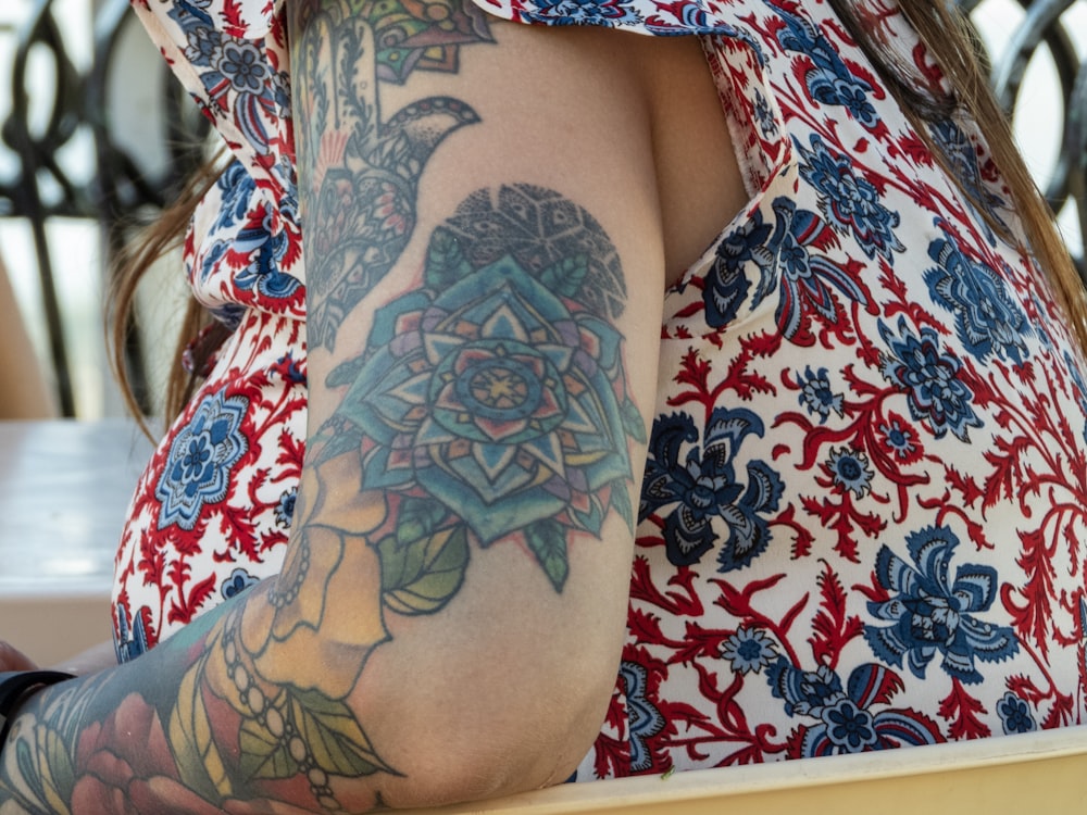 woman wearing red, blue, and white floral top with multicolored flower arm tattoo