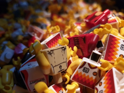 A close-up of a pile of LEGO minifigure parts, including torsos and arms. The pieces are brightly colored, primarily in reds, yellows, and whites with sporty patterns. The image is densely packed with details of the minifigure torsos.