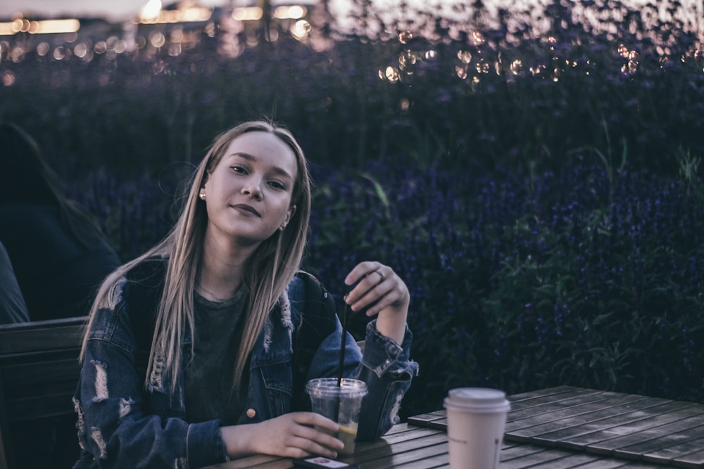 woman wearing distressed blue denim jacket near wooden table smiling