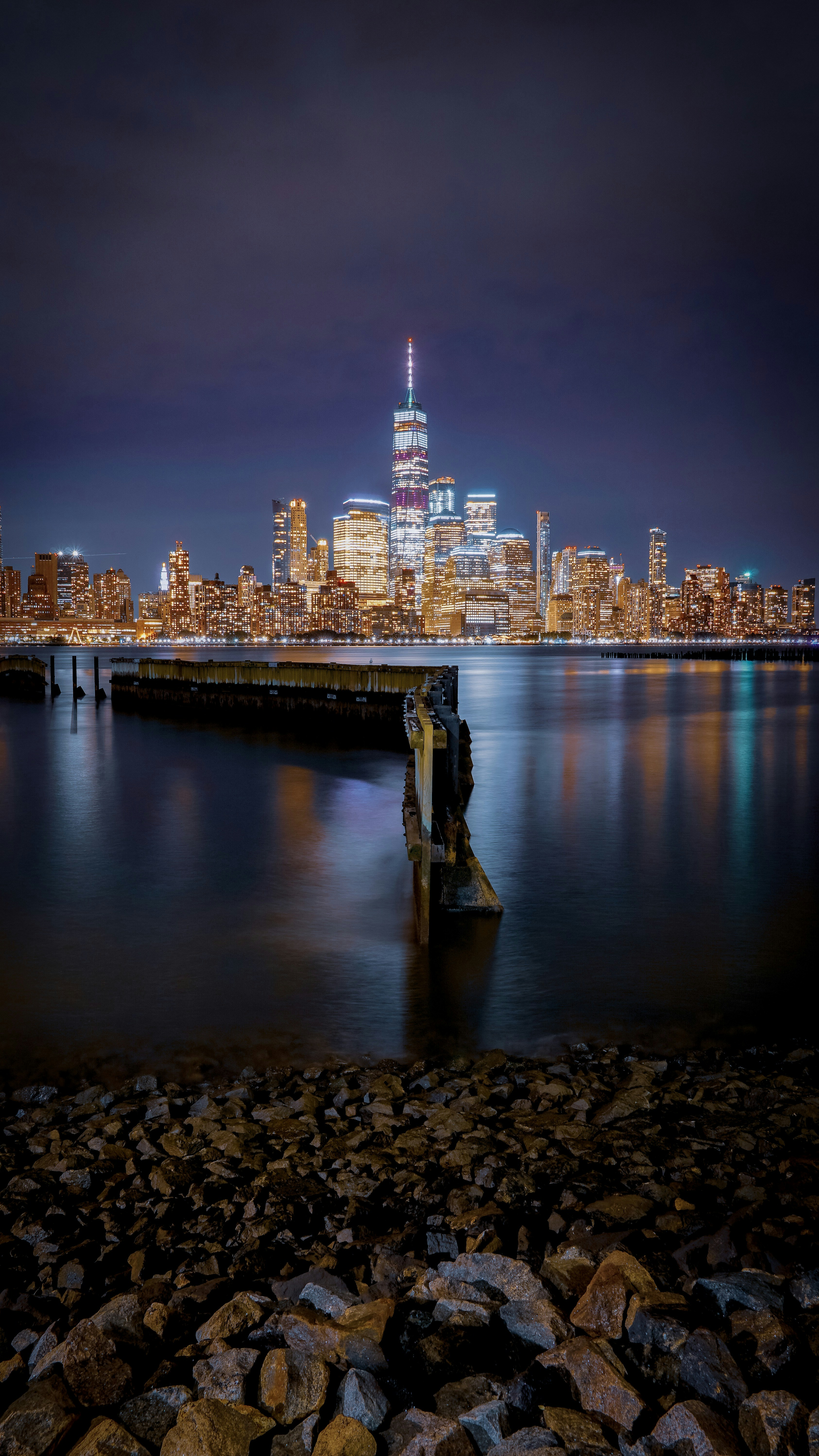 New York City skyline at night with glowing skyscrapers reflected in the East River, long-exposure cityscape photography