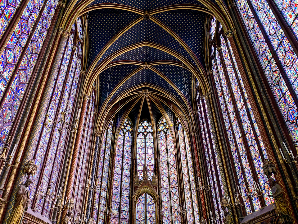 The image depicts a grand, Gothic-style church with a high vaulted ceiling and numerous stained glass windows that fill the interior with vibrant colors. The perspective is from below, looking up towards the towering structure, emphasizing its height and architectural beauty. The walls of the church are adorned with gold accents, adding to the overall opulence of the scene. The image does not contain any discernible text or countable objects, but rather focuses on the intricate details and grandeur of the cathedral-like space.

The stained glass windows, which cover a significant portion of the walls from floor to ceiling, are particularly striking due to their vivid colors and intricate designs. These windows serve as a testament to the craftsmanship and artistic prowess of the era in which they were created. The image does not contain any discernible actions or movements, but rather captures the stillness and tranquility of this magnificent architectural space.