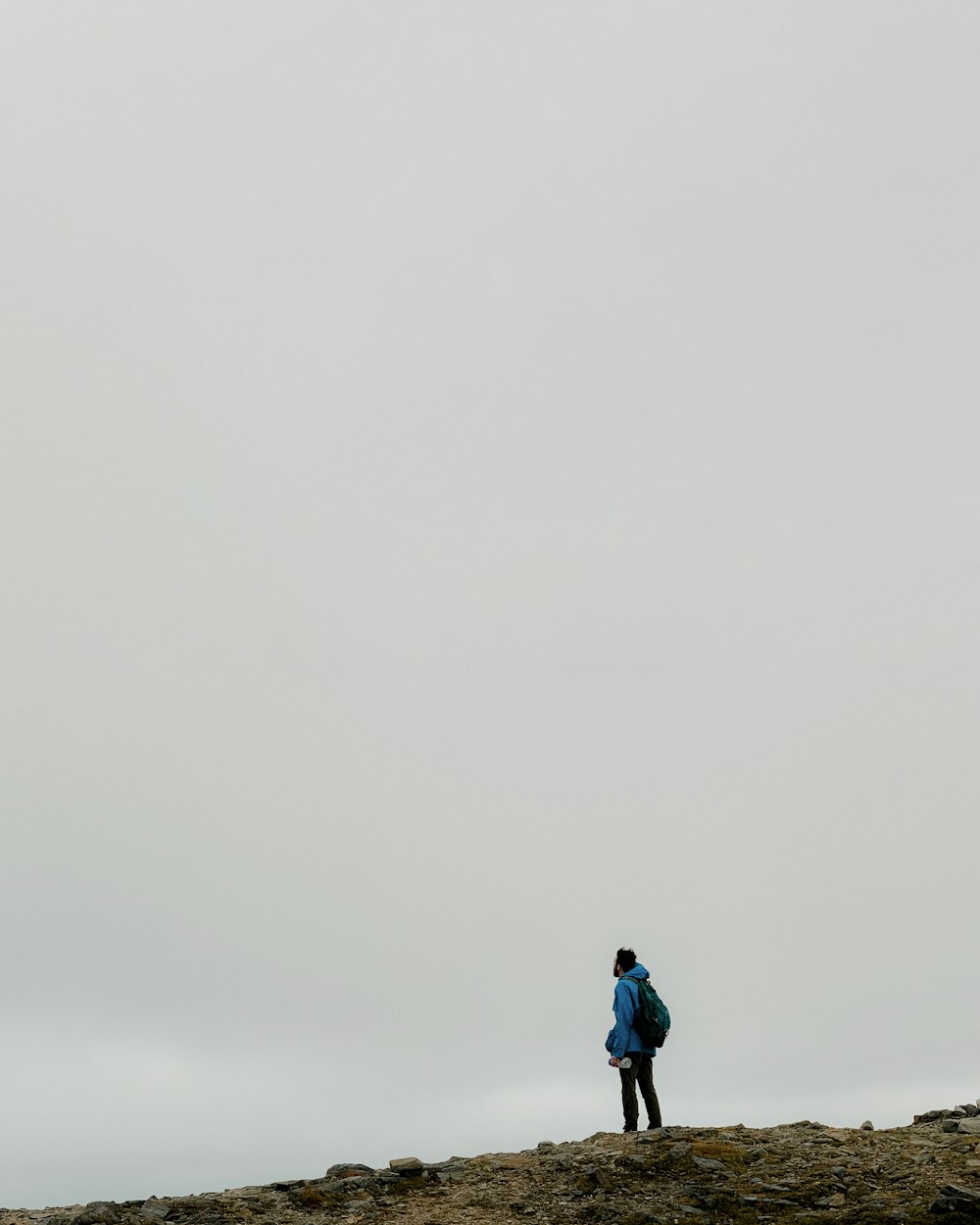 standing man wearing blue jacket on cliff during daytime